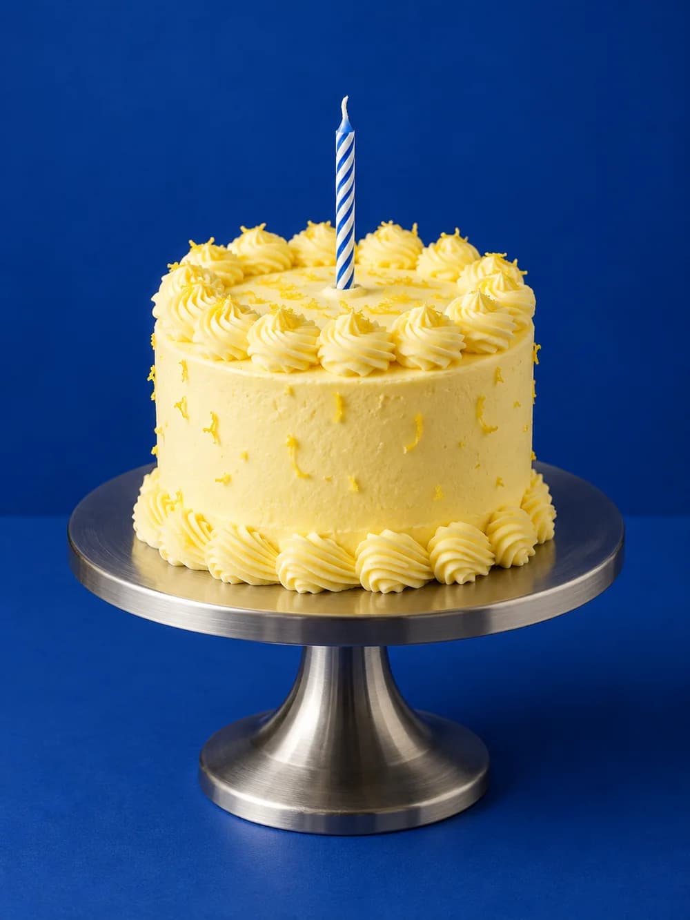 A lemon birthday cake with one candle on a metal pedestal